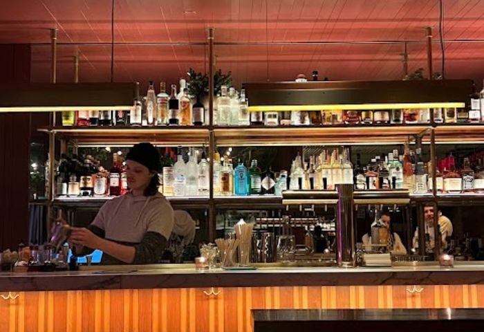 Bartender mixing drinks at a stylish bar in New York. Shelves of liquor bottles. Gay travel advice for nightlife and cool spots.