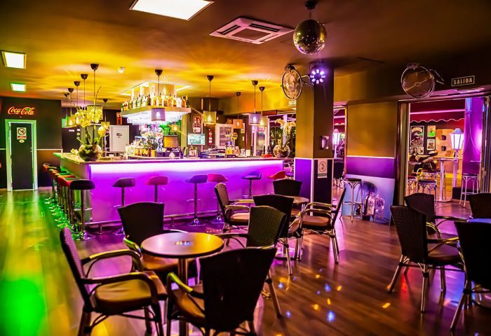 Interior of Na Und Bar, a gay bar in Gran Canaria. Features include a bar with purple lighting, tables, & chairs. Disco ball visible.