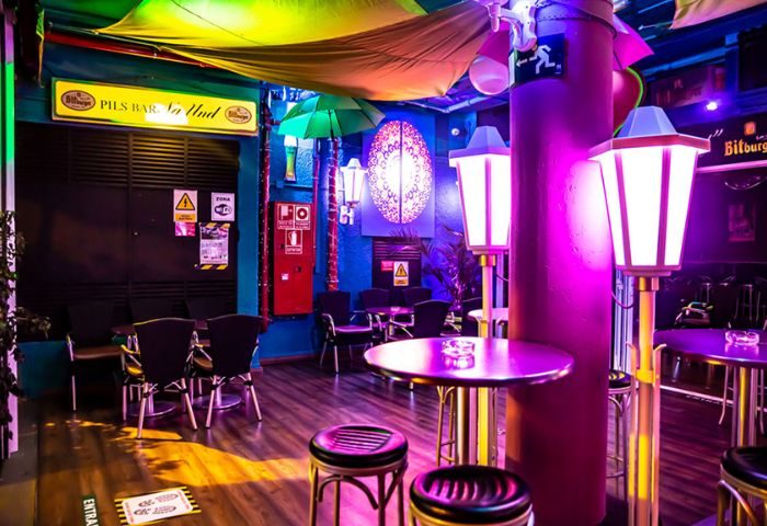 Interior of Na Und Bar, a gay bar in Gran Canaria. Tables, chairs, stools, and colorful lighting create a vibrant atmosphere.
