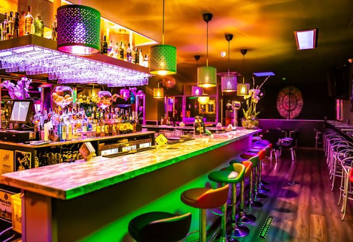 Interior of Na Und Bar, a gay bar in Gran Canaria. Colorful lights illuminate the bar, stools, and liquor bottles. Gay travel advice.