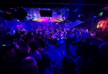 Never Mind Bar Copenhagen: A crowded gay bar with blue lighting and laser beams. Nightlife scene for gay men traveling in Copenhagen.