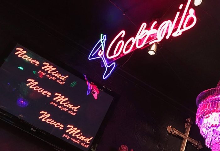 Never Mind Bar, Copenhagen. Neon 'Cocktails' sign, TV screen displaying the bar's name, and a chandelier in this gay night club.
