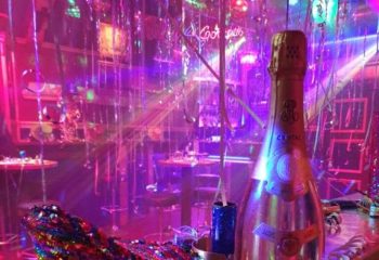 Never Mind Bar Copenhagen: Champagne bottle in a vibrant, festive gay bar setting with pink and purple lighting, perfect for gay men travel.