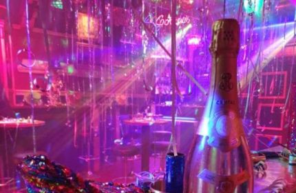 Never Mind Bar Copenhagen: Champagne bottle in a vibrant, festive gay bar setting with pink and purple lighting, perfect for gay men travel.