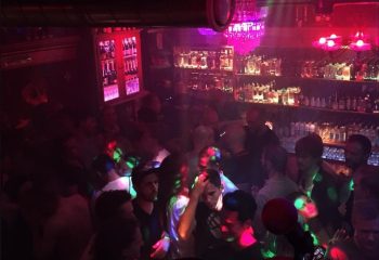 Crowded Never Mind Bar in Copenhagen. Gay bar scene with men, bar, bottles, and colorful lights. Gay travel advice.