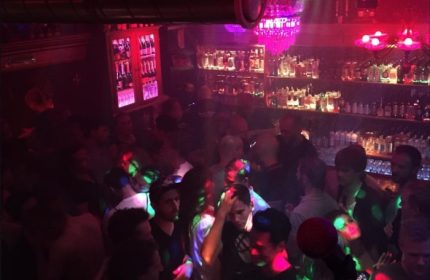 Crowded Never Mind Bar in Copenhagen. Gay bar scene with men, bar, bottles, and colorful lights. Gay travel advice.