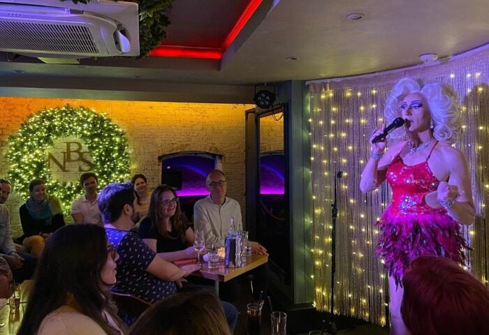 New Bloomsbury Set: Drag show at a cosy gay bar in London. Drag queen performing on stage for an audience during a quiz night.