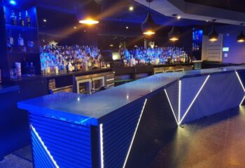 Interior of Incognito Gay Bar in Benidorm. Bar with blue lighting, liquor bottles, and modern design. Gay travel destination.