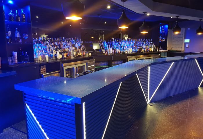 Interior of Incognito Gay Bar in Benidorm. Bar with blue lighting, liquor bottles, and modern design. Gay travel destination.