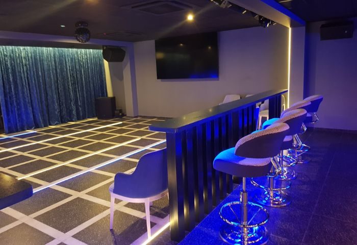 Interior of New Incognito Gay Bar in Benidorm. Blue lighting, bar stools, dance floor, stage with curtains, and TV screen. Gay travel.