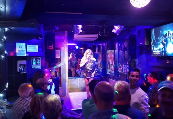 Drag queen performing at New People gay bar in Benidorm, Spain. Crowd watching show with disco ball and blue lighting. Gay travel.