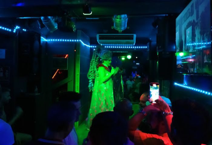 Drag queen performing at New People gay bar in Benidorm. Nightlife scene with people watching, neon lights, and vibrant atmosphere.