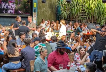 Patio scene at Newtown Hotel, Sydney. People at tables, enjoying drinks & live music. Gay travel destination, vibrant atmosphere.