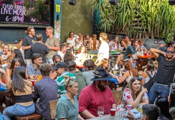 Patio scene at Newtown Hotel, Sydney. People at tables, enjoying drinks & live music. Gay travel destination, vibrant atmosphere.