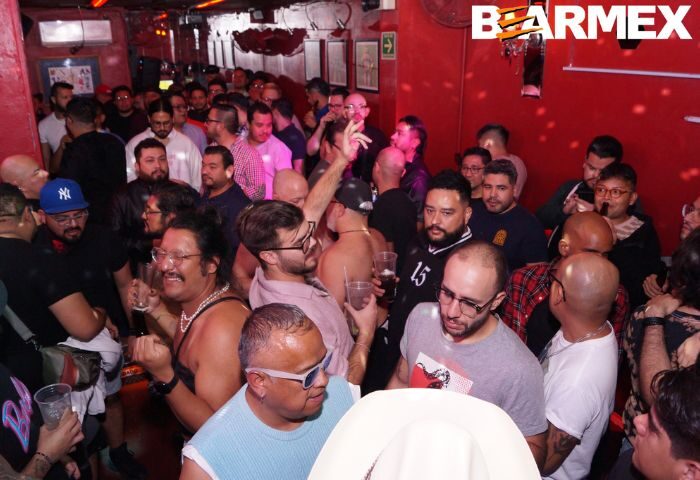 Crowded Nicho Bears Bar gay party in Mexico. Many men enjoying drinks, dancing, and socializing in a vibrant, red-lit atmosphere. Gay travel.