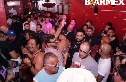 Crowded Nicho Bears Bar gay party in Mexico. Many men enjoying drinks, dancing, and socializing in a vibrant, red-lit atmosphere. Gay travel.