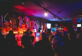 Night Barcelona Gay Cruise Club interior. Crowded bar scene with red and blue lighting, balloons, and patrons enjoying the nightlife.
