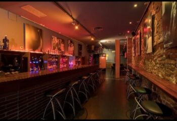 Night Barcelona Gay Cruise Club Interior. Bar with stools, bottles, and artwork. A popular gay bar in Barcelona for gay men travel.