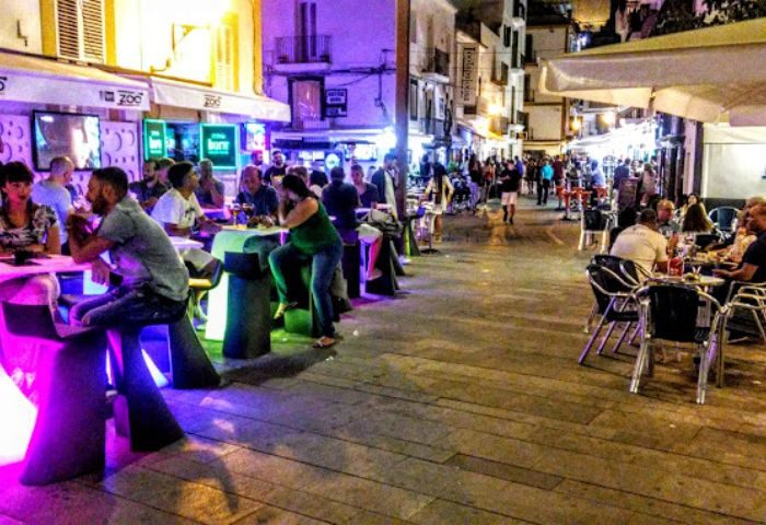 Night view of Nini Ibiza Bar, a popular gay bar and party spot. People sit at tables, enjoying drinks in the vibrant atmosphere.