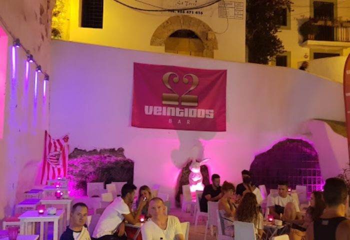 Gay bar Veintidoos in Ibiza. People sit at tables under pink lights. Nini Ibiza Bar, a gay party spot, is a popular travel destination.