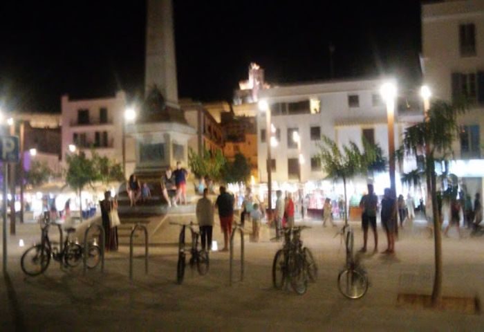 Night view of Ibiza gay bar. People walk around the square. Bicycles are parked. Ibiza gay party scene.