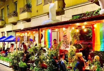 NoLoSo Bar in Milan: Outdoor seating area with rainbow flags, plants, and an inflatable unicorn. A gay-friendly travel destination.