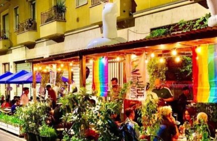 NoLoSo Bar in Milan: Outdoor seating area with rainbow flags, plants, and an inflatable unicorn. A gay-friendly travel destination.