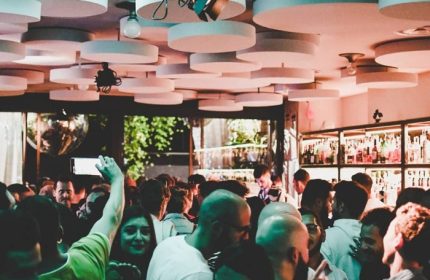 Crowded NoLoSo Bar in Milan. Gay bar scene with people, unique ceiling design, and bar shelves. Gay travel advice.