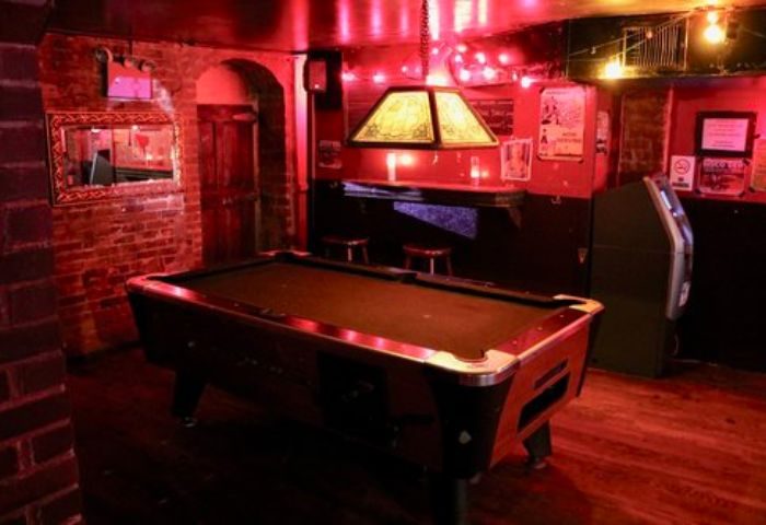Nowhere Bar in New York: A dimly lit gay bar with a pool table, brick walls, and red lighting. A popular travel destination for gay men.