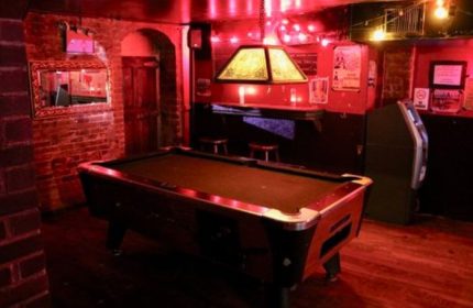 Nowhere Bar in New York: A dimly lit gay bar with a pool table, brick walls, and red lighting. A popular travel destination for gay men.