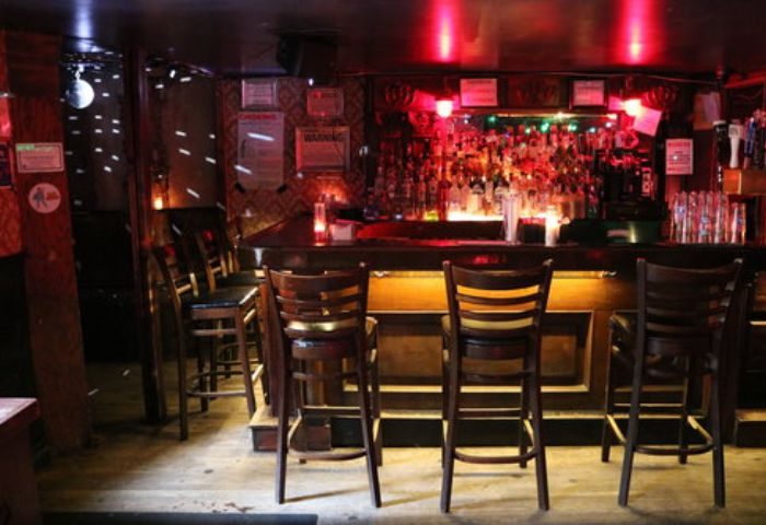 Interior of Nowhere Bar in New York. Bar stools line the counter, with a disco ball and red lighting creating a vibrant atmosphere. Gay travel.