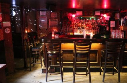Interior of Nowhere Bar in New York. Bar stools line the counter, with a disco ball and red lighting creating a vibrant atmosphere. Gay travel.