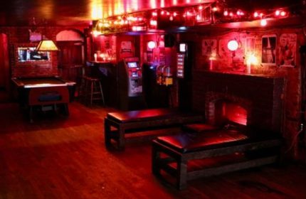 Nowhere Bar in New York City. Red lighting, pool table, benches, fireplace, arcade games. Gay bar travel advice, nightlife.