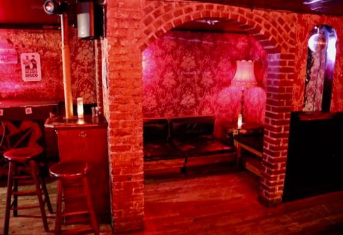 Nowhere Bar in New York. Red-lit interior with brick archway, wallpaper, bar stools, and disco ball. A gay travel destination.