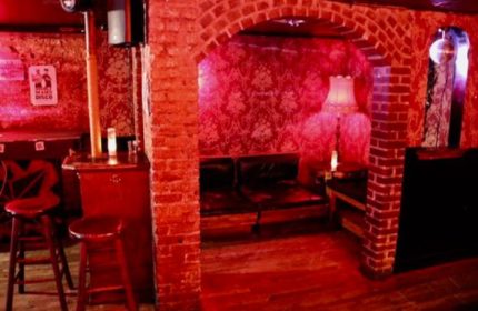 Nowhere Bar in New York. Red-lit interior with brick archway, wallpaper, bar stools, and disco ball. A gay travel destination.