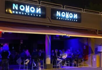 Noxon Club, a gay cruise club in Gran Canaria. The club's sign is visible above the entrance, with people seated at the bar.