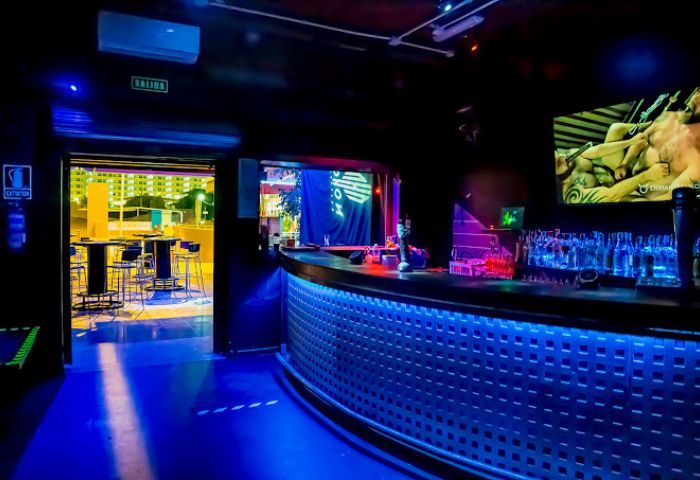 Interior of Noxon Club, a gay cruise club in Gran Canaria. Blue lighting illuminates the bar and dance floor. Tables visible outside.