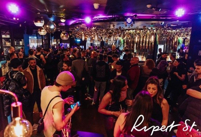 Interior of Rupert Street Bar, a gay bar in London's Soho. Disco balls hang from the ceiling above a crowded room. Gay nightlife.