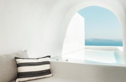 Armenaki Santorini hotel rooftop pool view. Gay hotels list travel guide. White architecture, blue sea, striped pillow. Gay travel.