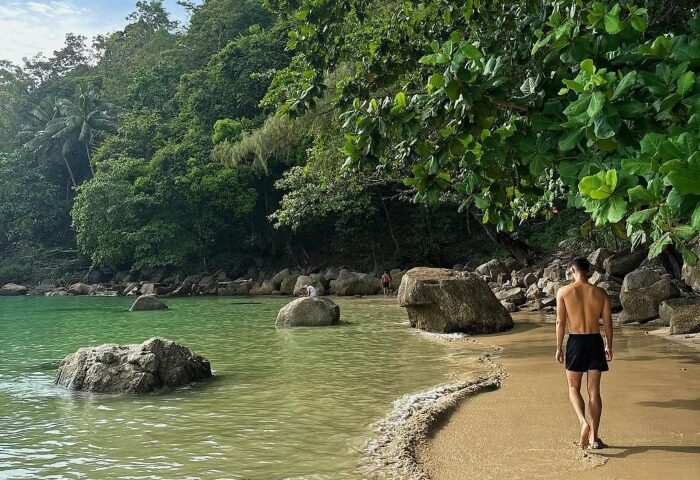 Man walking on the beach at InterContinental Phuket Resort, a luxury gay hotel. Beachfront view with lush greenery and turquoise water.