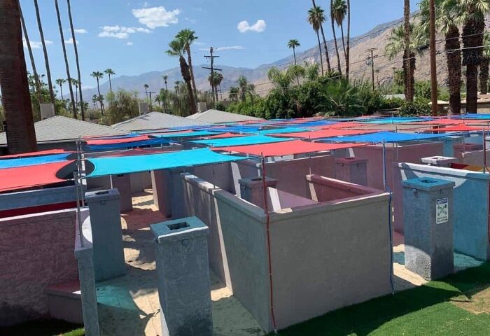 All Worlds Resorts and Annex, a clothing-optional gay men's resort in Palm Springs. Cabanas with blue and red shades. Palm trees in background.