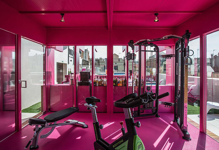 TWO Hotel Barcelona by Axel, adults-only gay hotel gym. Pink interior with exercise equipment, bar, and pool view. Gay travel in Barcelona.