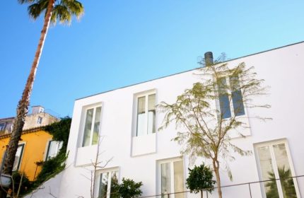 The Late Birds Lisbon, a gay-friendly hotel. White building with windows, palm tree, and blue sky. Gay urban resort architecture.