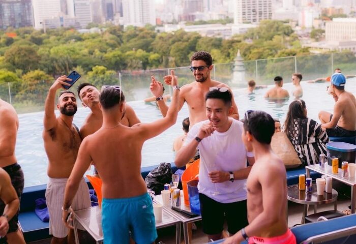 Gay Bangkok rooftop pool party at WHY SO/ bar. Men enjoy drinks and selfies. Number one gay-friendly spot for a night out in Thailand.
