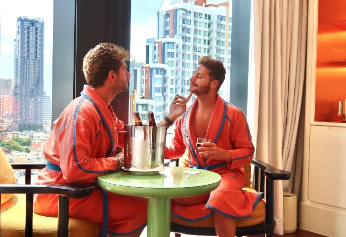 Gay Honeymoon at The Standard, Bangkok Mahanakhon. Two men in robes enjoy drinks with a city view. Luxury gay travel in Thailand.