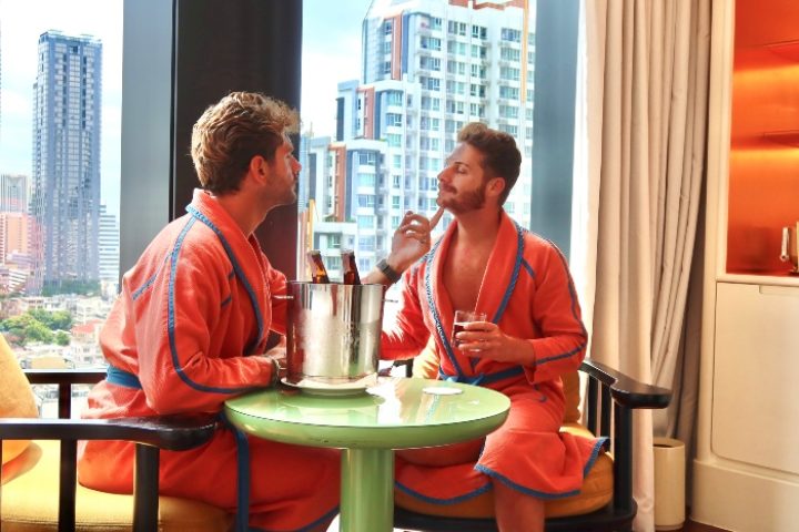 Gay Honeymoon at The Standard, Bangkok Mahanakhon. Two men in robes enjoy drinks with a city view. Luxury gay travel in Thailand.