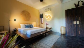 Bedroom at Rambutan Resort, Siem Reap. Honeymoon suite interior with king-size bed, wooden accents, and stylish decor. Gay-friendly hotel.