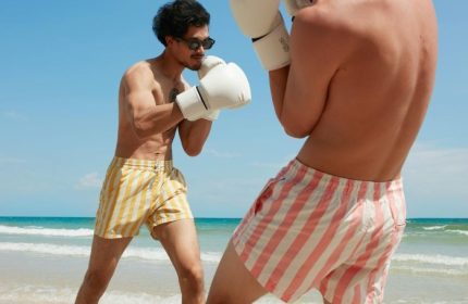 Gay honeymoon at The Standard Hua Hin. Two men boxing on the beach, wearing swim trunks and boxing gloves. Gay travel advice.