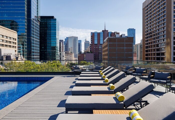 Le Meridien Melbourne rooftop pool. Gay hotel in Melbourne's gayborhood with city skyline views. Loungers and chairs on deck.