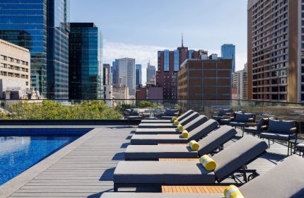 Le Meridien Melbourne rooftop pool. Gay hotel in Melbourne's gayborhood with city skyline views. Loungers and chairs on deck.